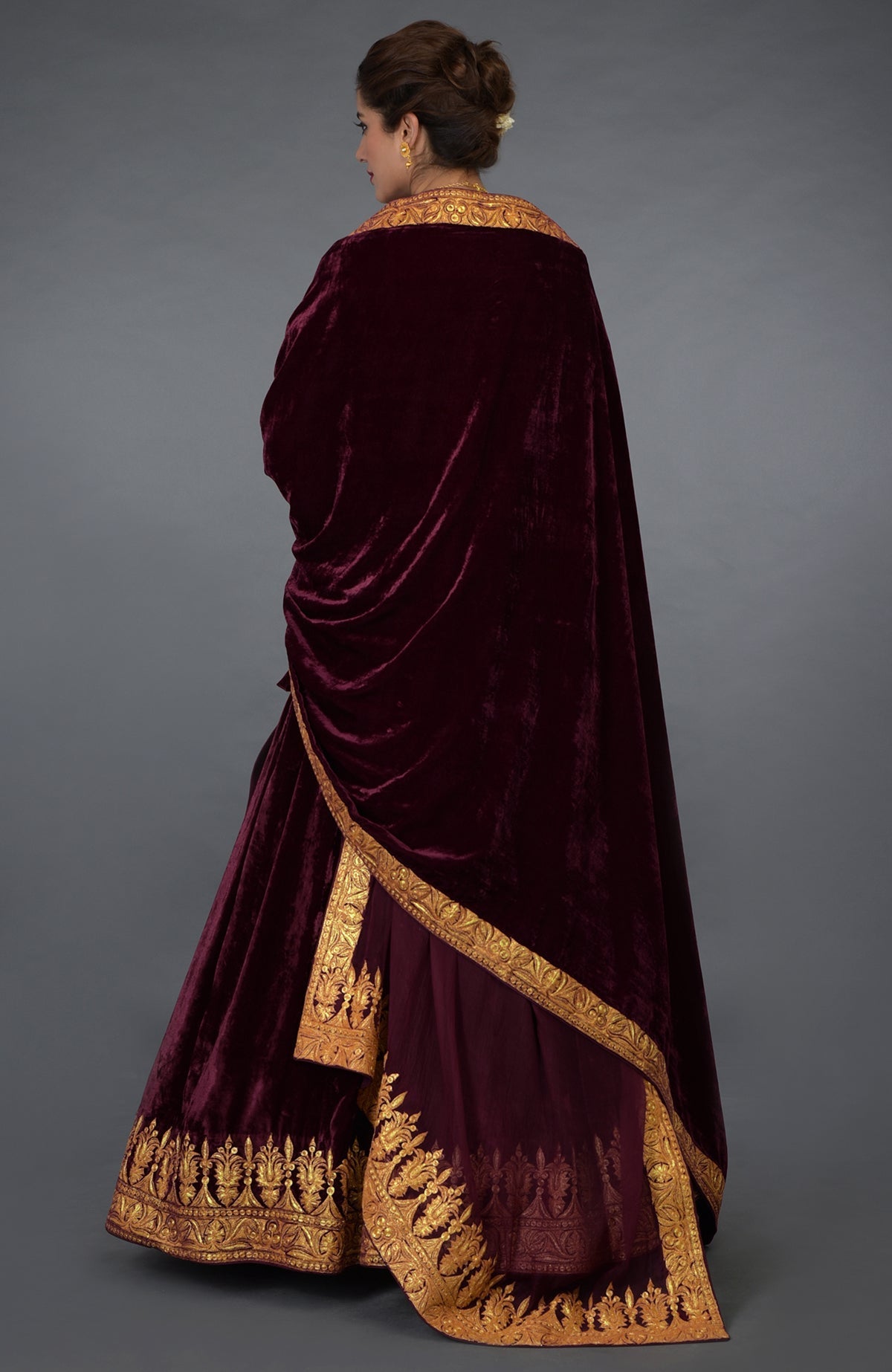 A woman models a burgundy velvet lehenga outfit with gold tilla embroidery.