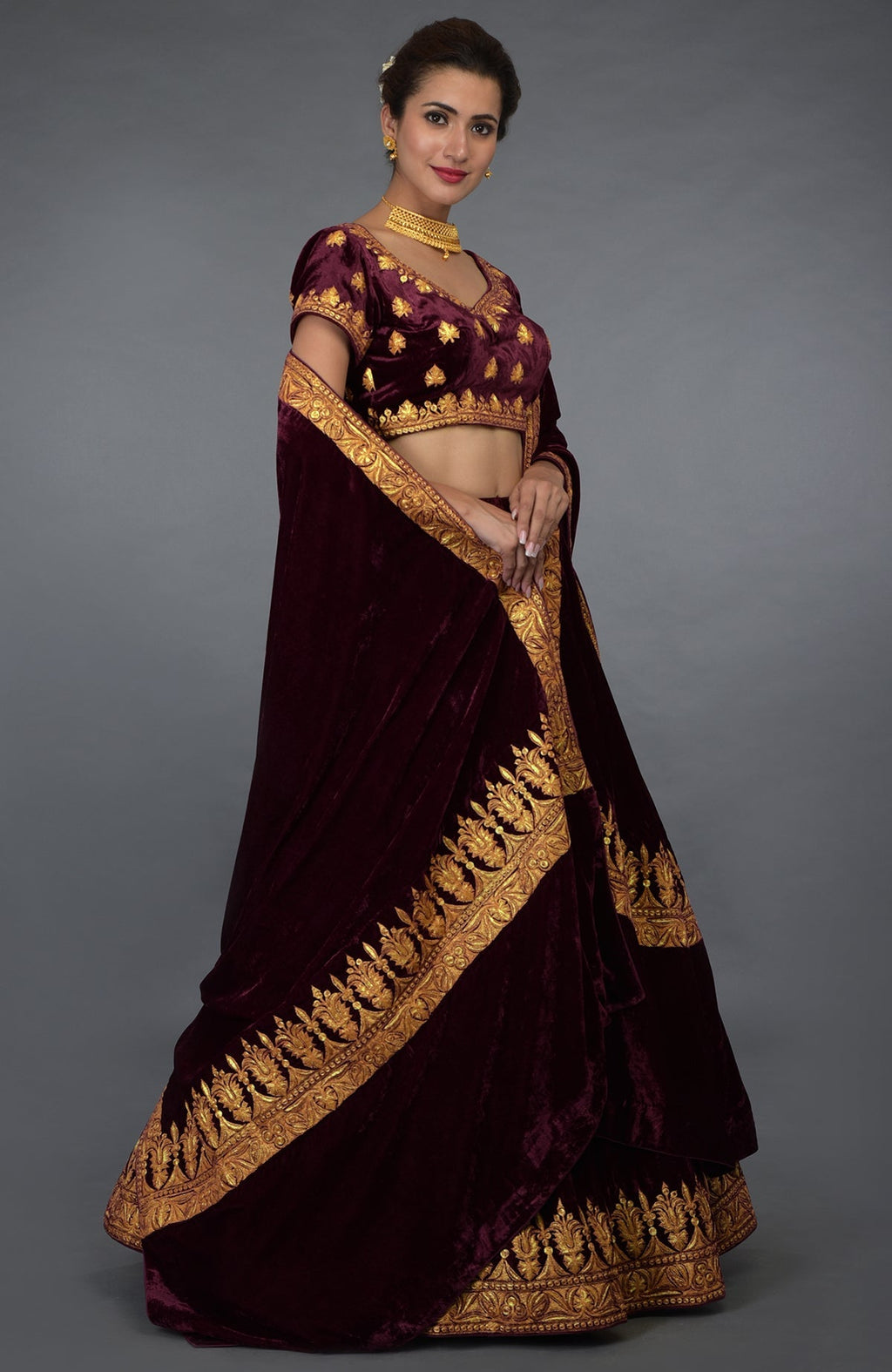 A woman models a burgundy velvet lehenga with gold tilla embroidery.