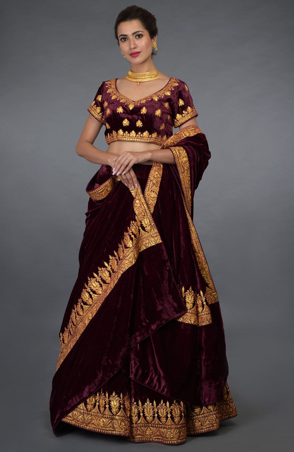 A woman models a burgundy velvet lehenga with gold tilla embroidery.
