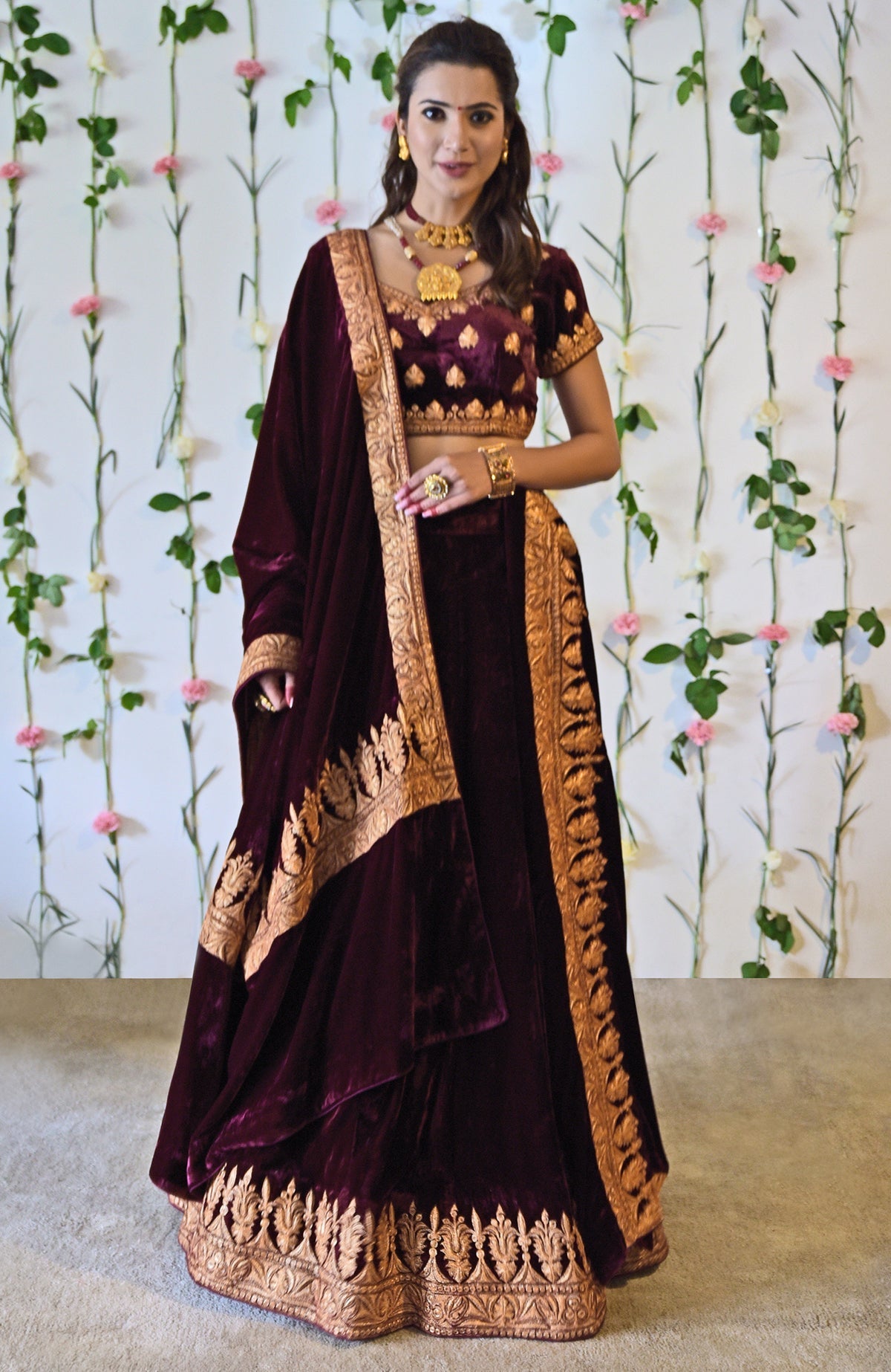 A woman models a burgundy velvet lehenga with gold tilla embroidery.