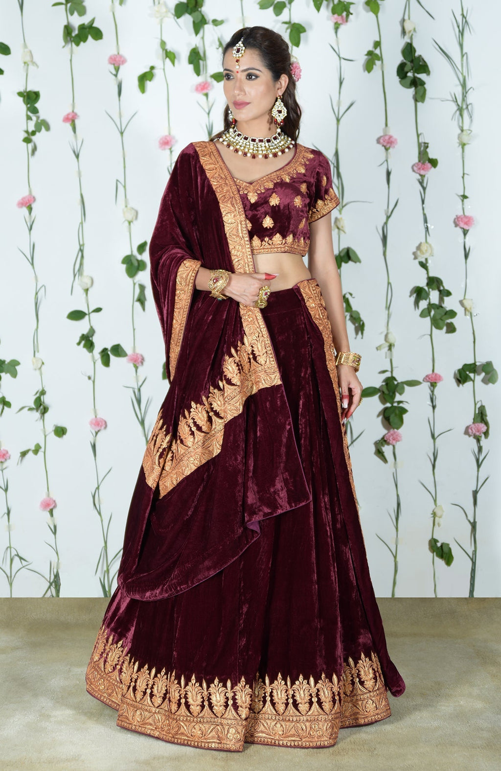 A woman models a burgundy velvet lehenga with gold tilla embroidery.