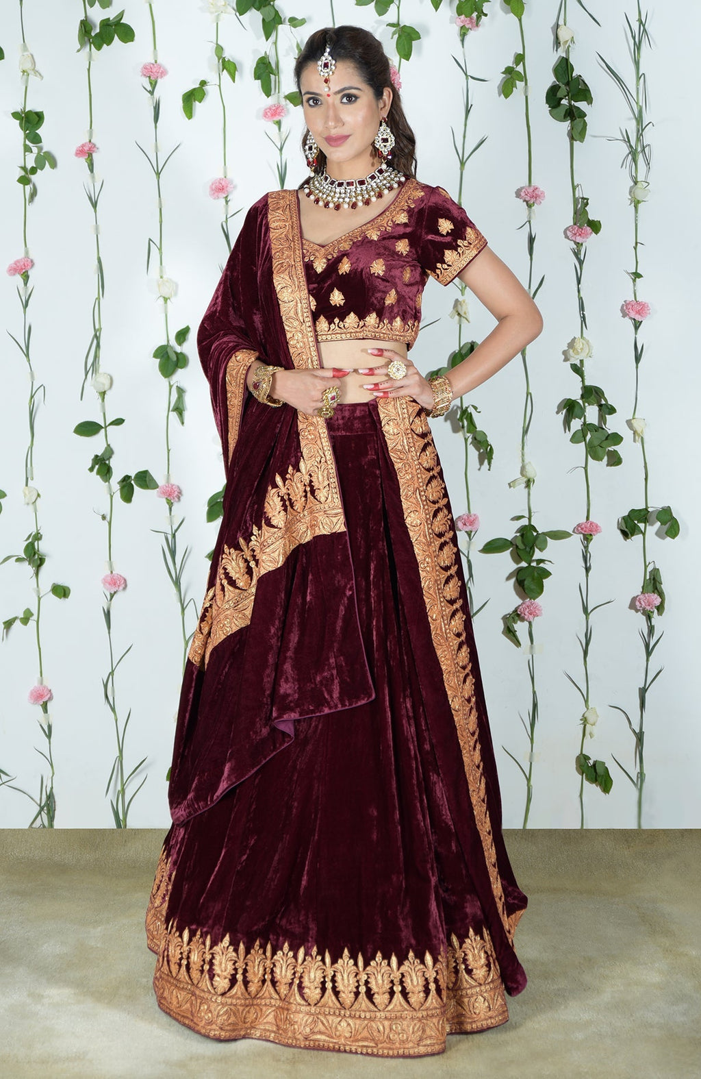 A woman models a burgundy velvet lehenga with gold tilla embroidery.