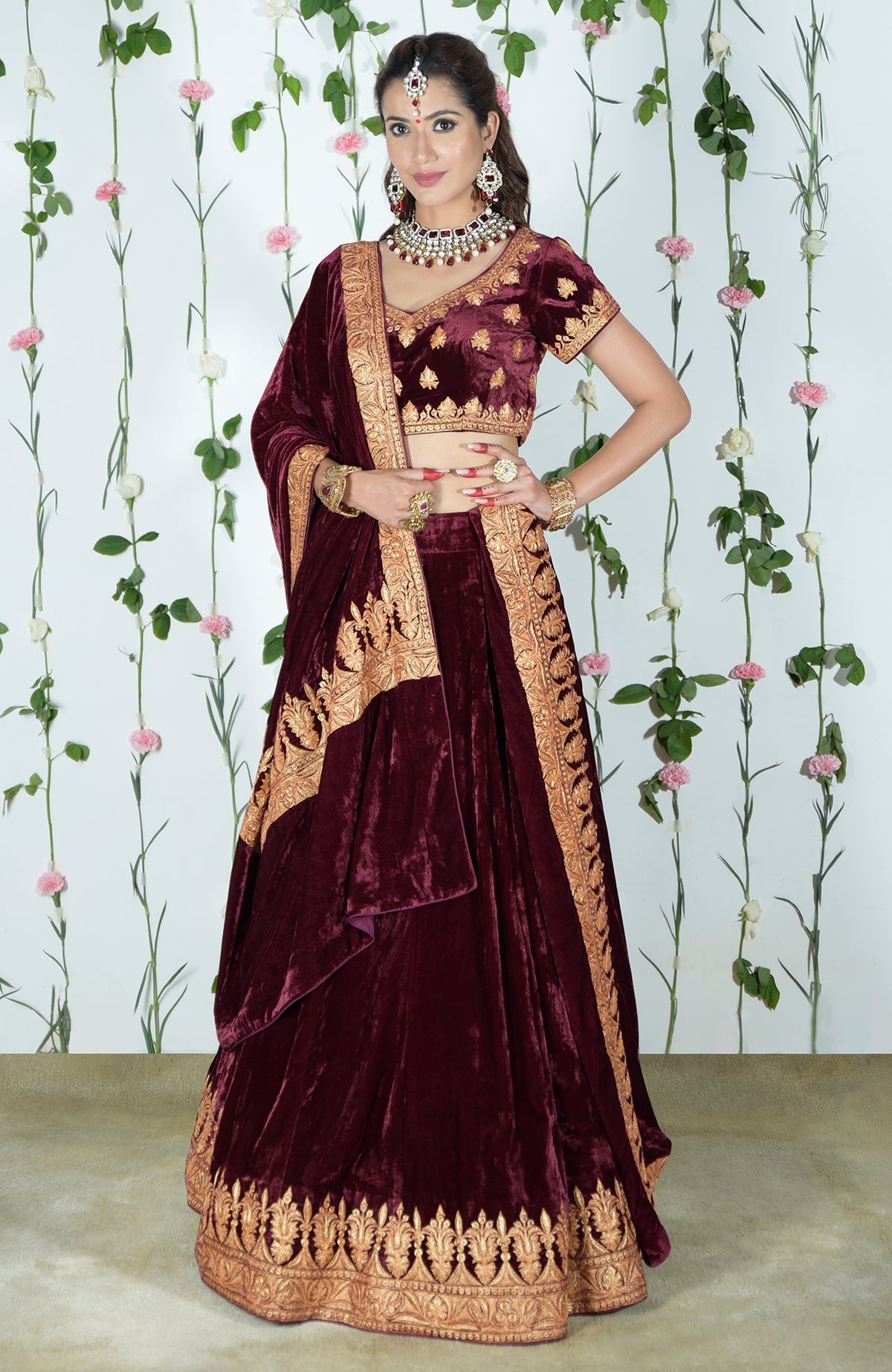 A woman models a burgundy velvet lehenga with gold tilla embroidery.