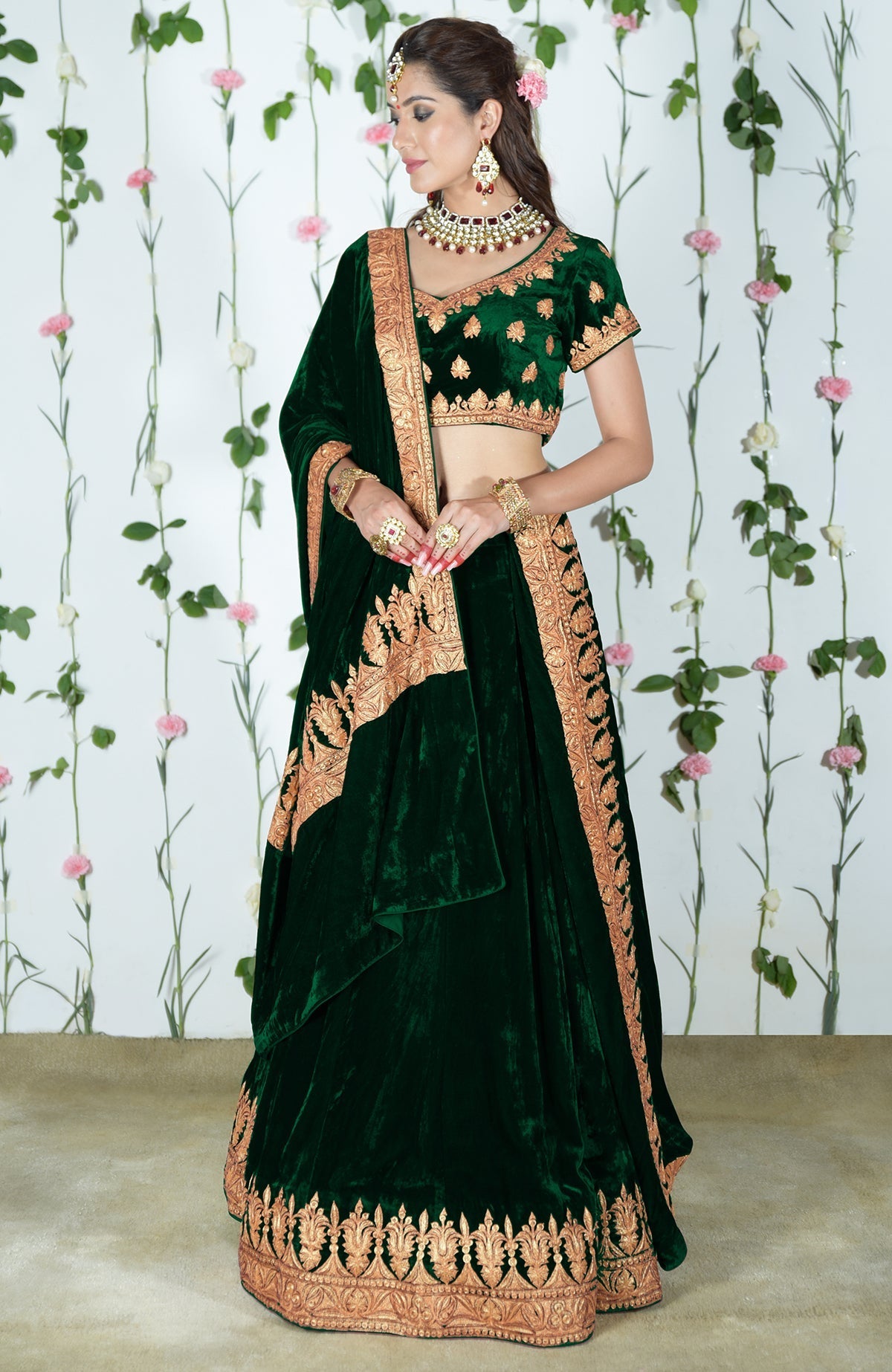An Indian woman models an emerald green velvet lehenga with gold tilla embroidery.