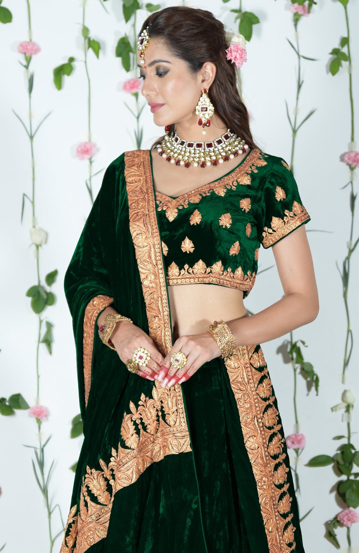 Emerald green velvet lehenga with gold tilla embroidery, worn by a woman.