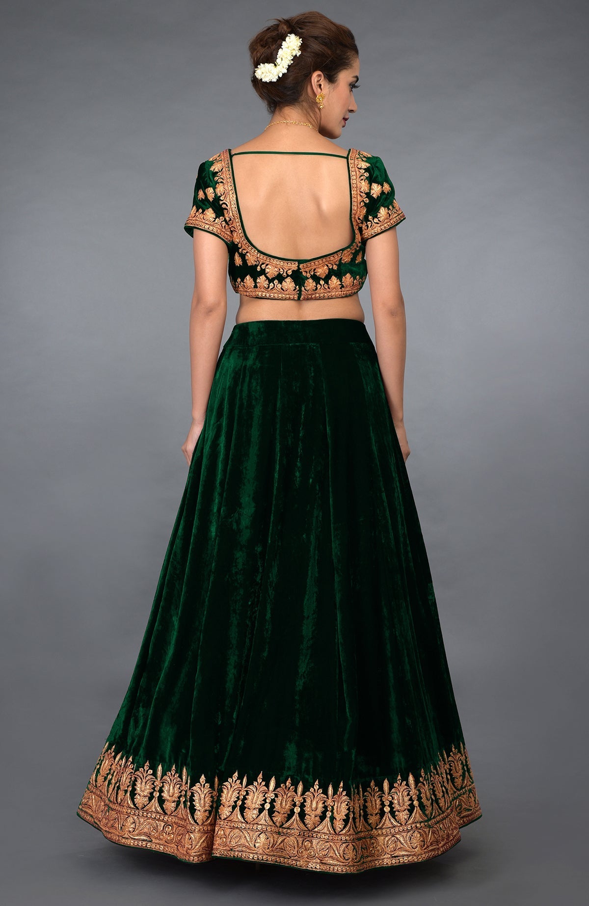 A woman models an emerald green velvet lehenga with gold tilla embroidery.