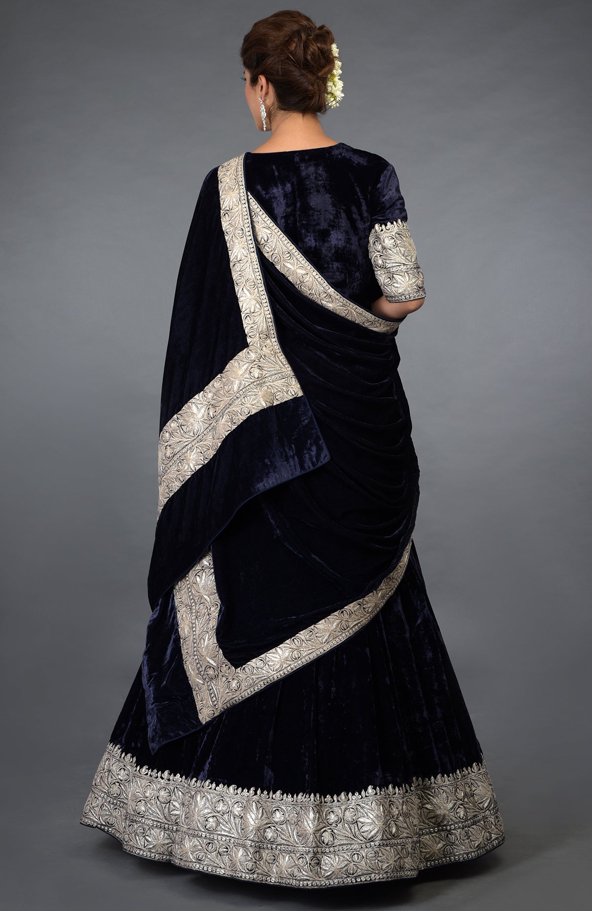 A woman models a midnight blue velvet lehenga with silver tilla embroidery.