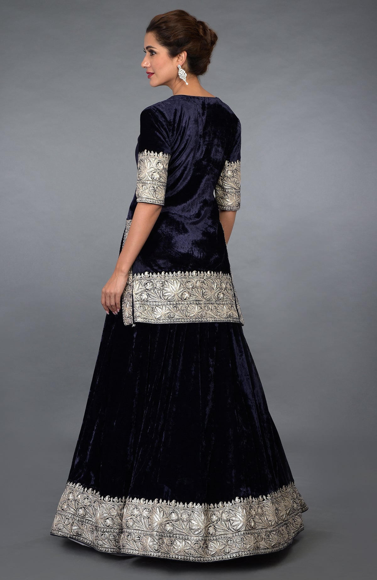 A woman models a midnight blue velvet lehenga with silver Kashmiri Tilla embroidery.