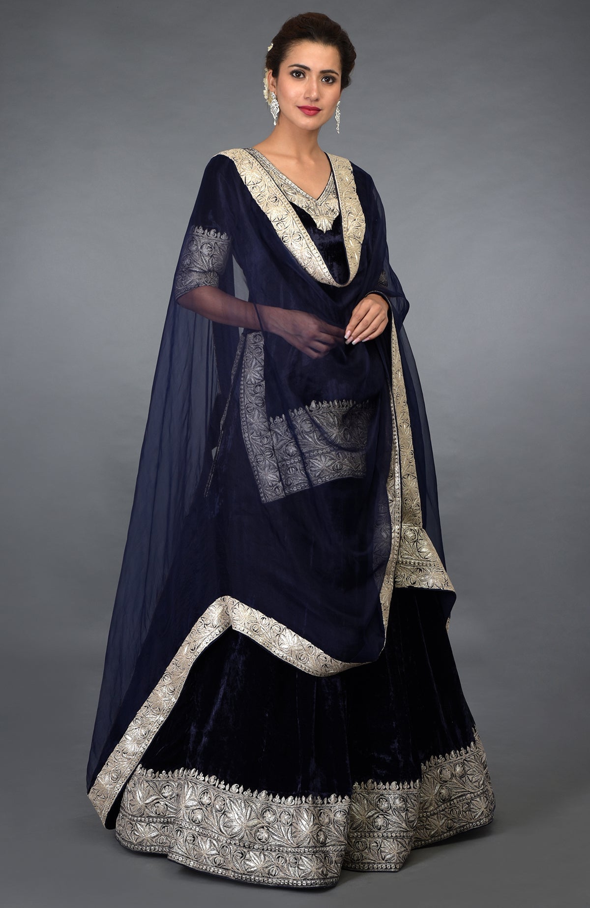 A woman models a midnight blue velvet lehenga with silver tilla embroidery.