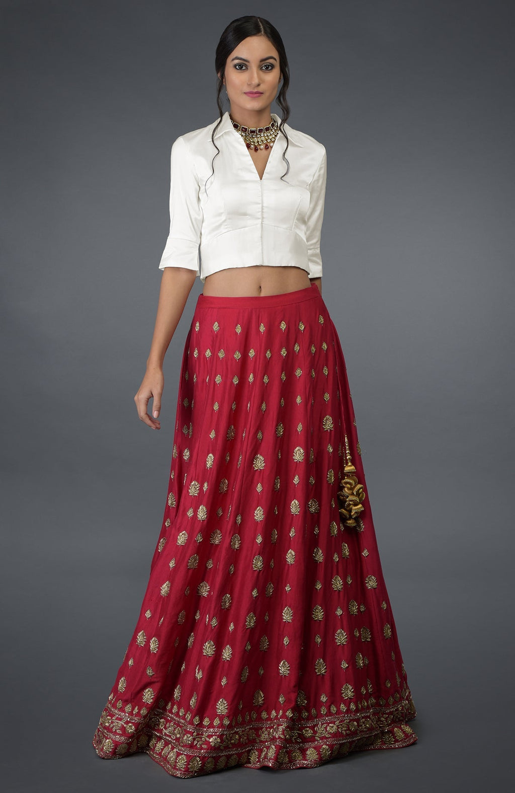 A woman models a red skirt with gold embroidery and a white crop top.