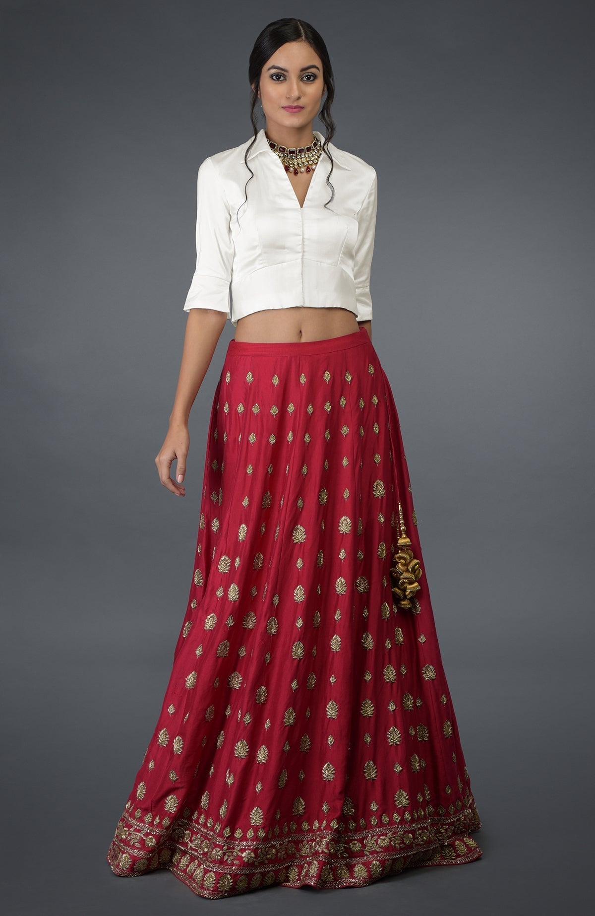 A woman models a red skirt with gold embroidery and a white crop top.
