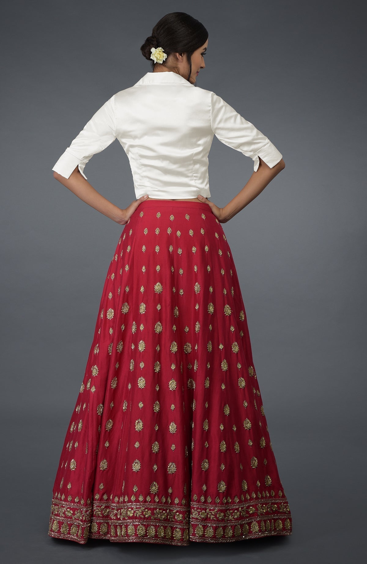 A woman models a red embroidered skirt and white satin blouse from the back.