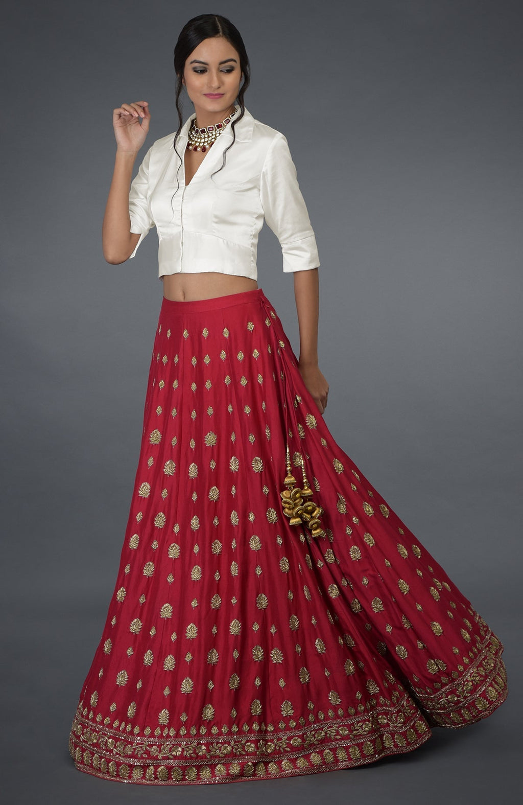 A woman models a red embroidered skirt with a white collared blouse and a necklace.