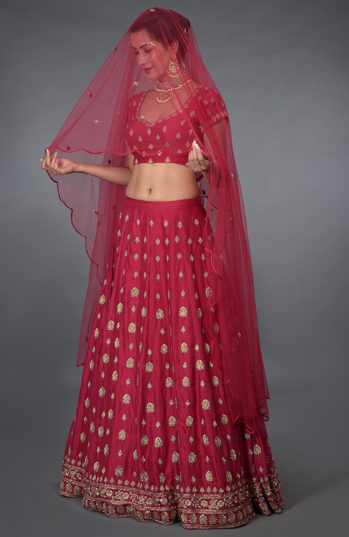A woman models a royal red Zardozi and crystal hand-embroidered lehenga outfit.