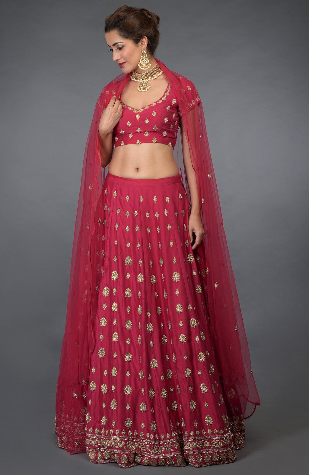 A woman models a royal red Zardozi and crystal hand-embroidered lehenga outfit.