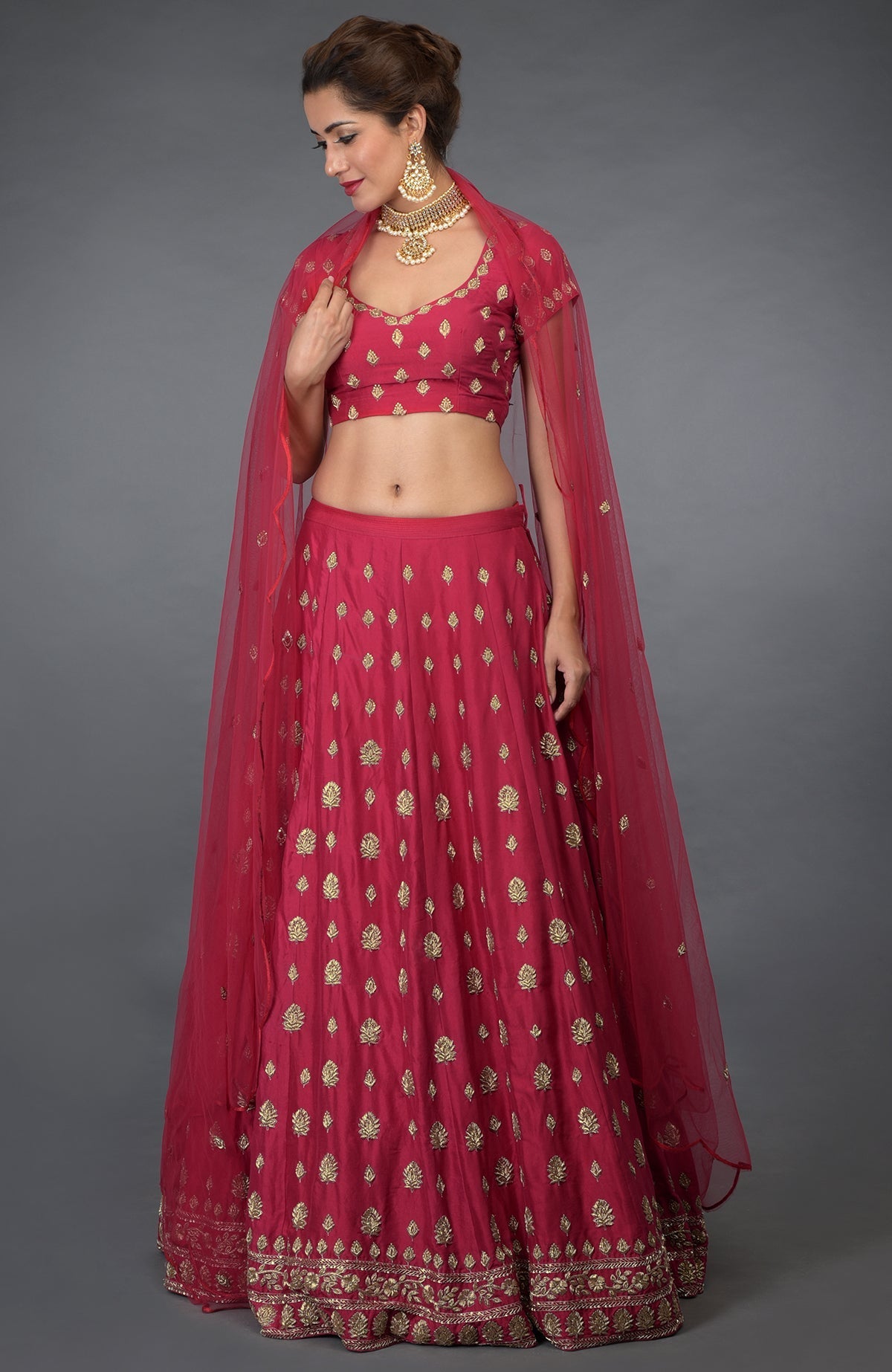 A woman models a royal red Zardozi and crystal hand-embroidered lehenga outfit.