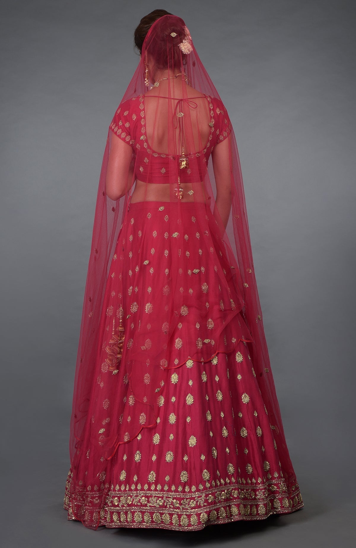 A woman from behind wearing a red embroidered lehenga with a sheer dupatta.