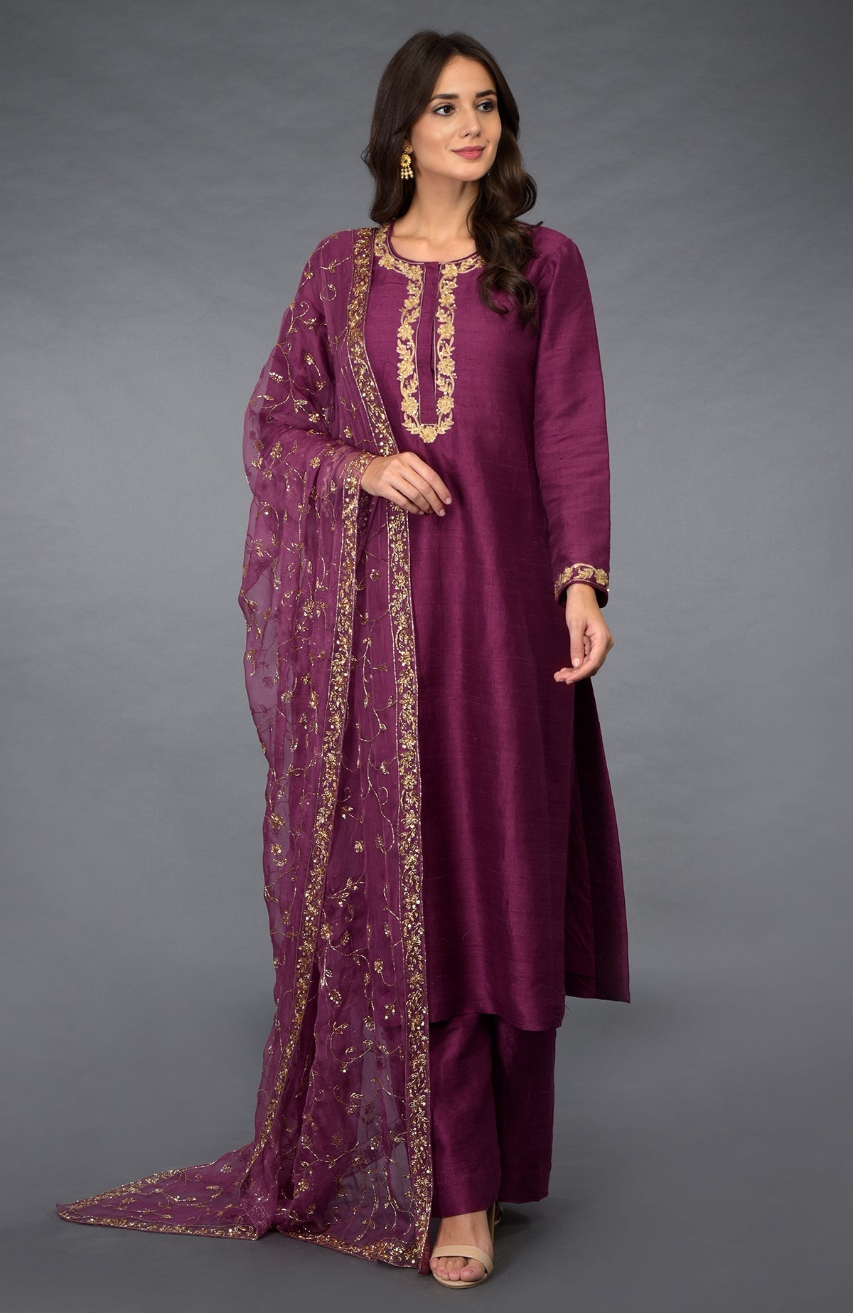 A woman models a peacock pink suit with gold zari, beads, and sequin embroidery.