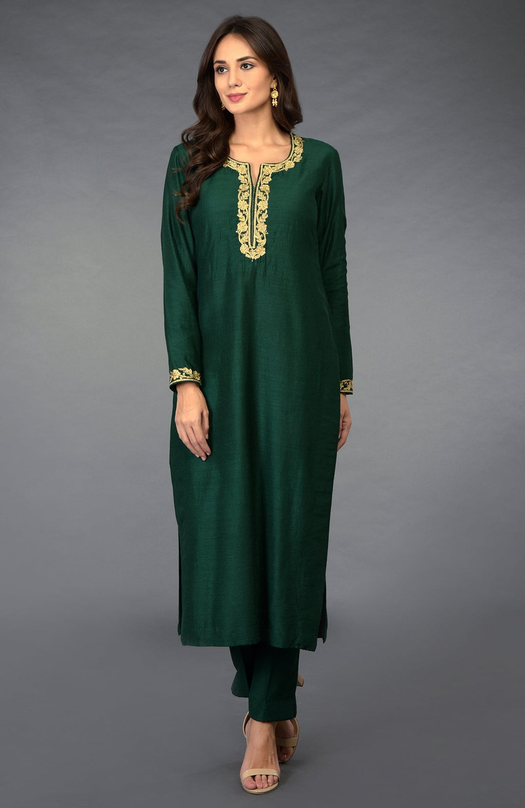 An elegant woman models an emerald green suit with gold embroidery on the neckline and cuffs.