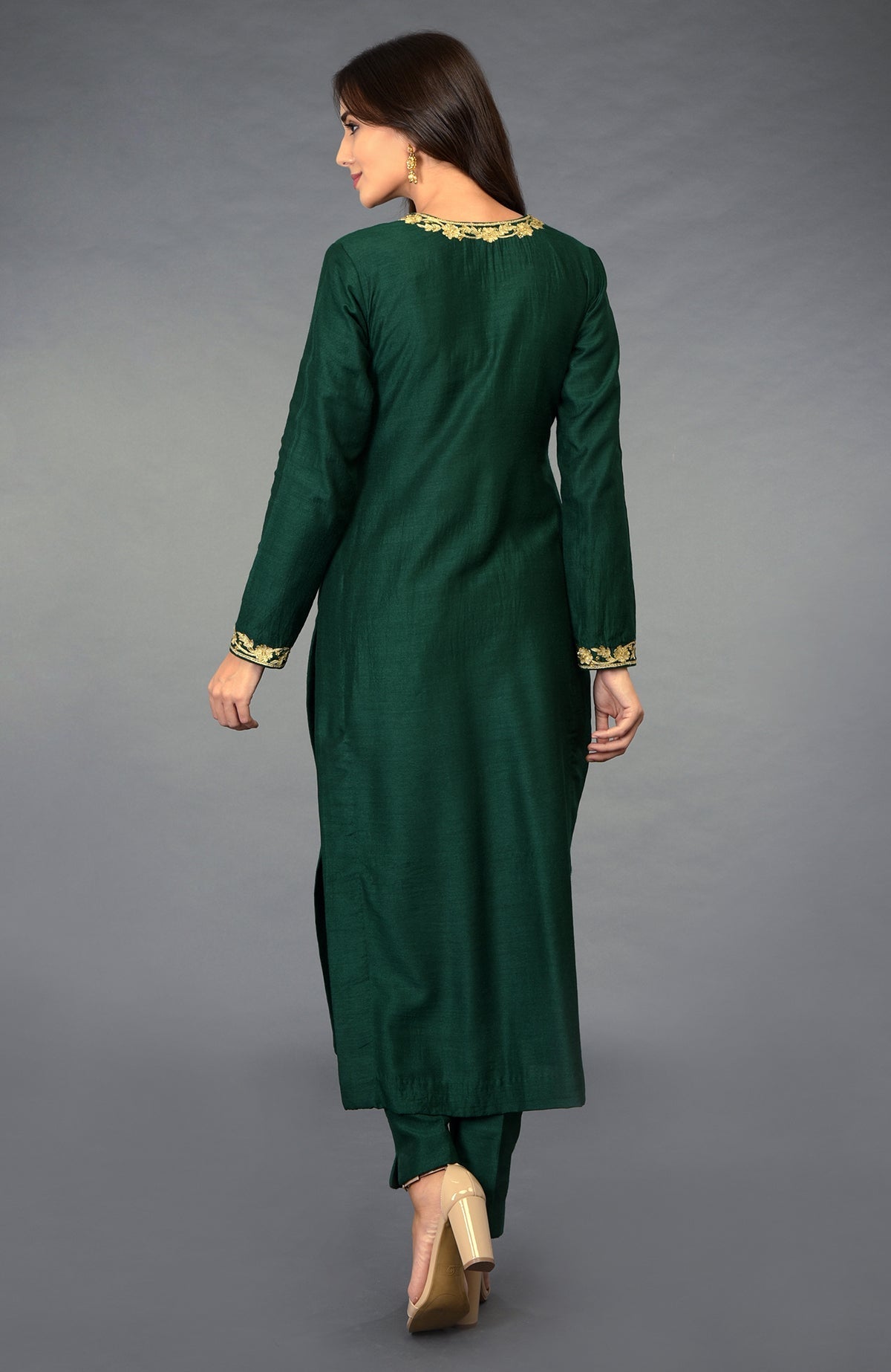A woman models an emerald green suit with gold embroidery on the neckline and cuffs.