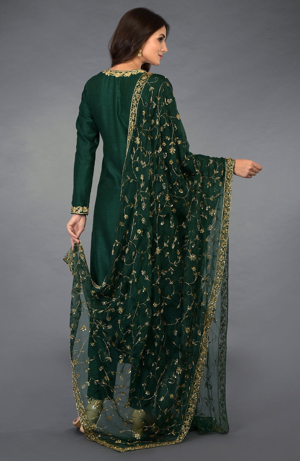 A woman models an emerald green suit with gold zari, beads, and sequin embroidery.