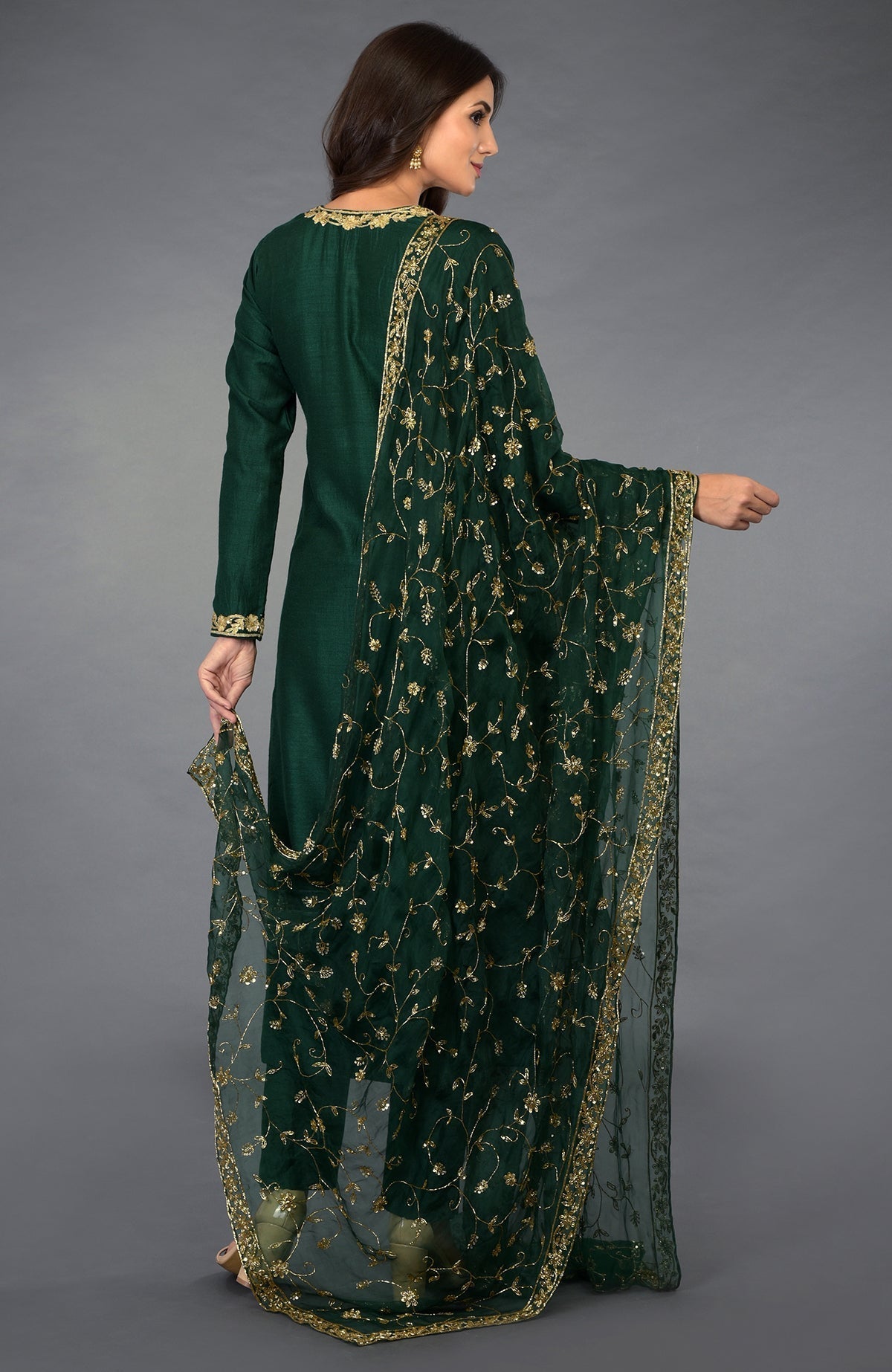 A woman models an emerald green suit with gold zari, beads, and sequin embroidery.