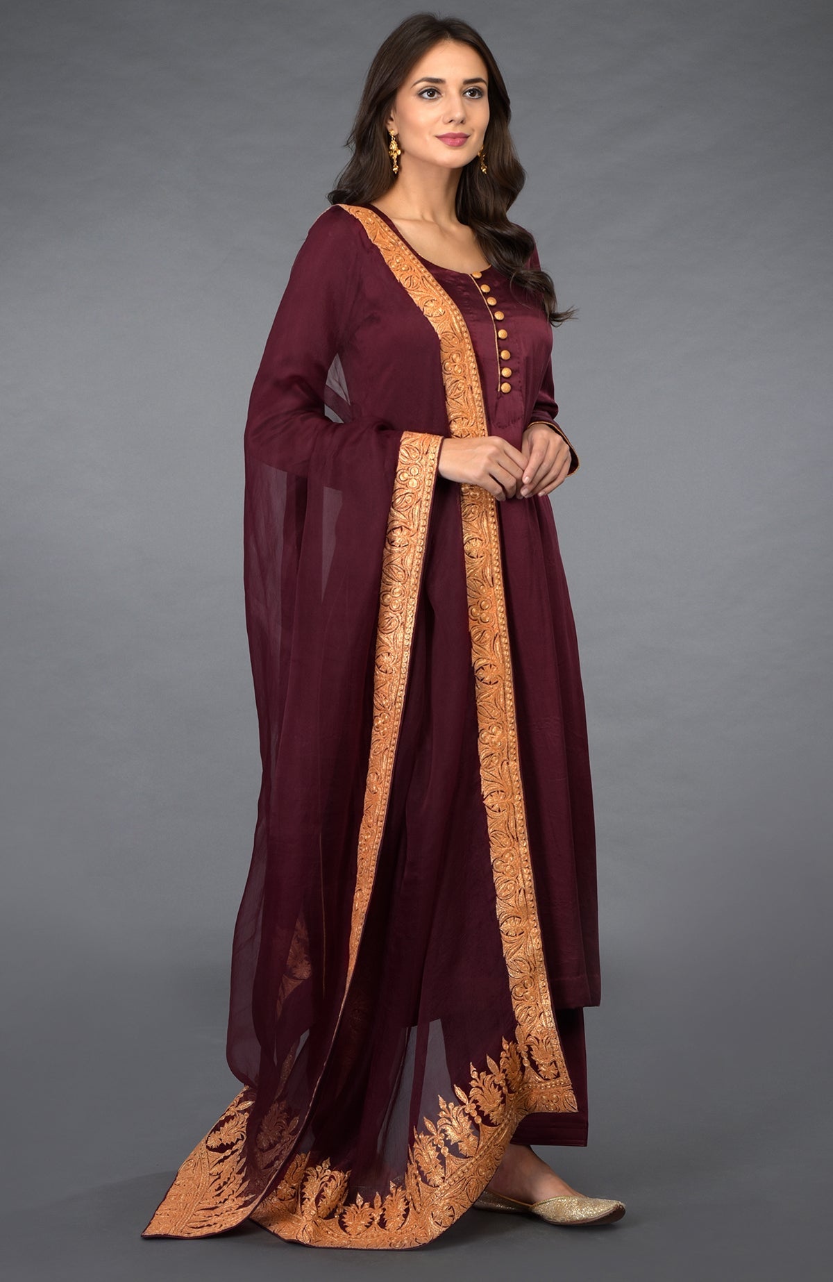 A woman models a burgundy salwar pants suit with gold tilla embroidery.