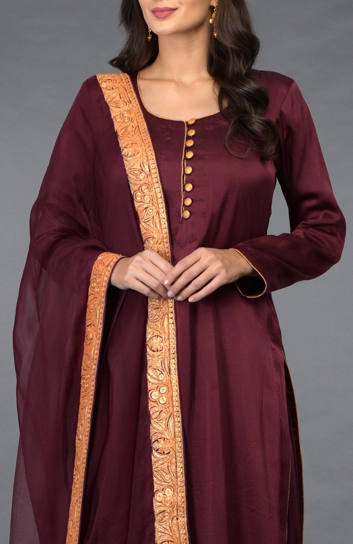 A woman models a burgundy salwar pants suit with gold tilla embroidered dupatta.