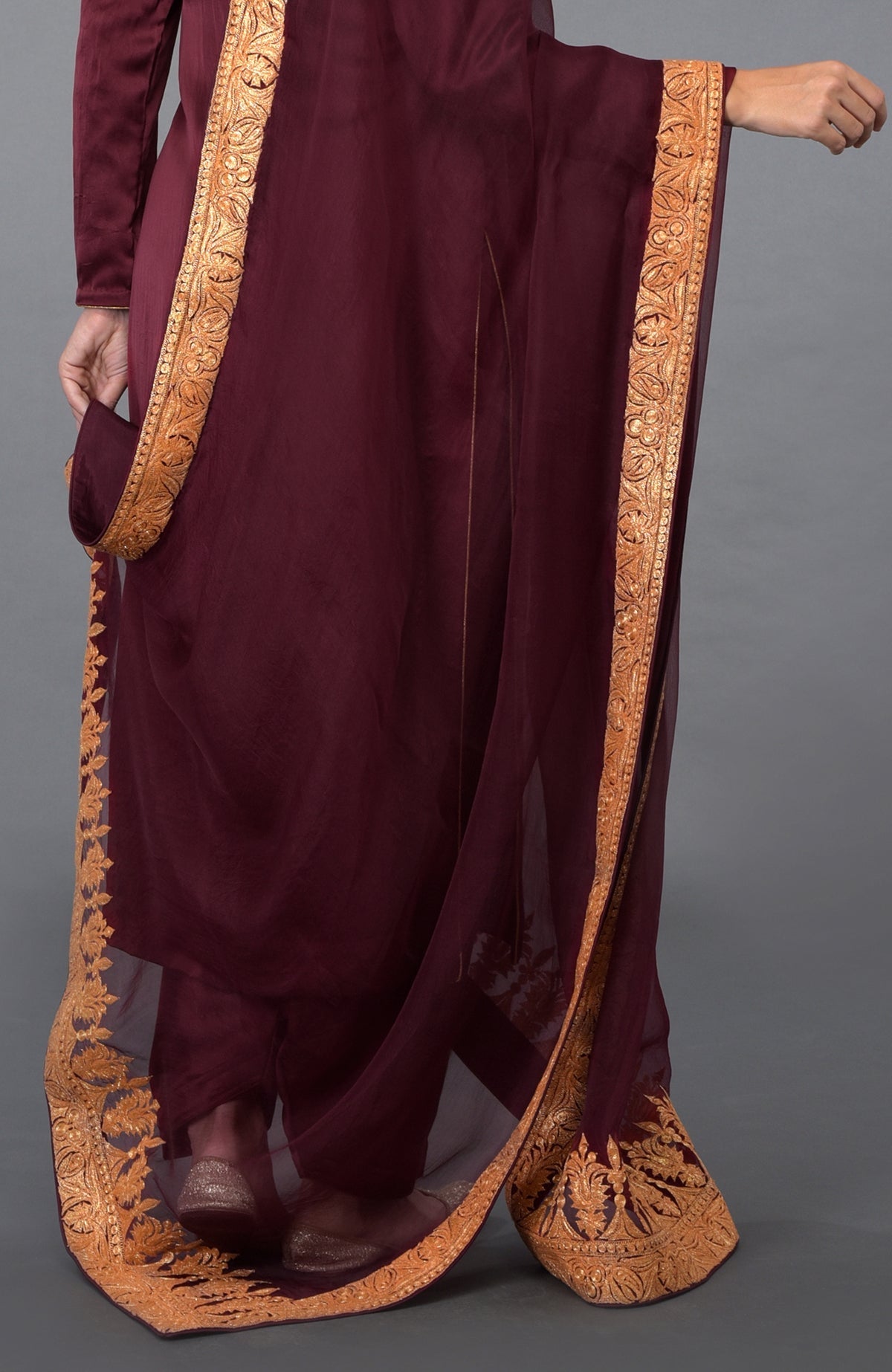 A woman models a burgundy salwar suit with a gold embroidered organza dupatta.