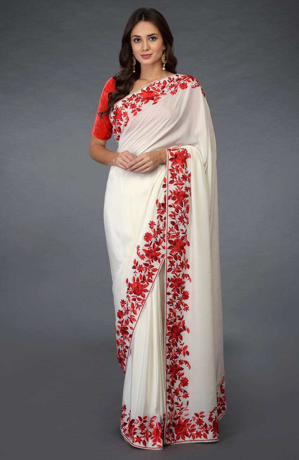 An elegant woman models an ivory saree with red floral embroidery and a red blouse.