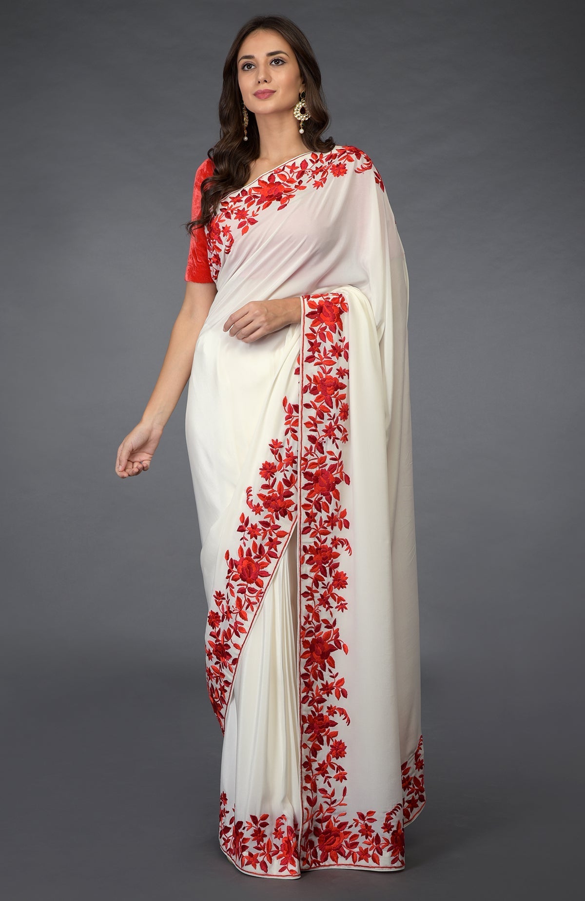 An elegant woman models an ivory saree with red floral Parsi Gara embroidery.
