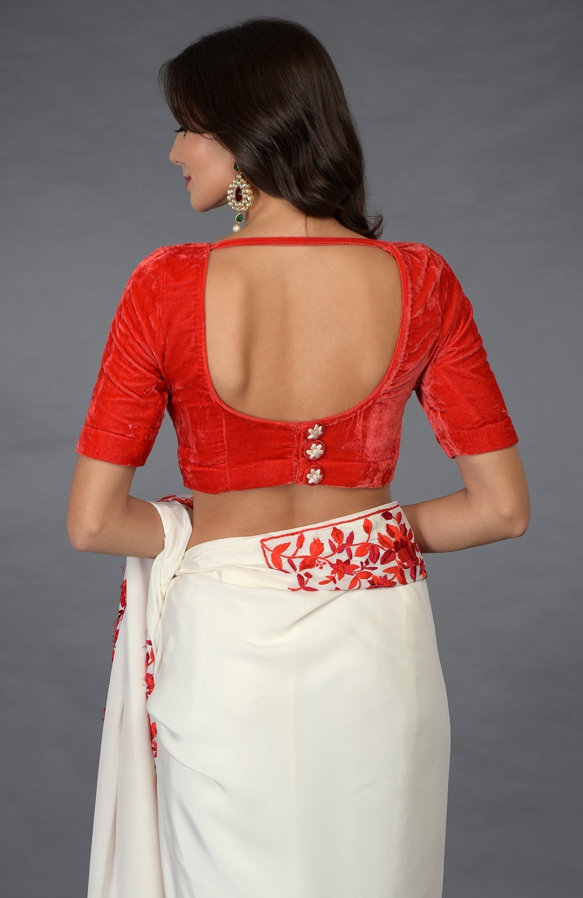 A woman from the back wearing a red velvet blouse and an ivory saree with red embroidery.