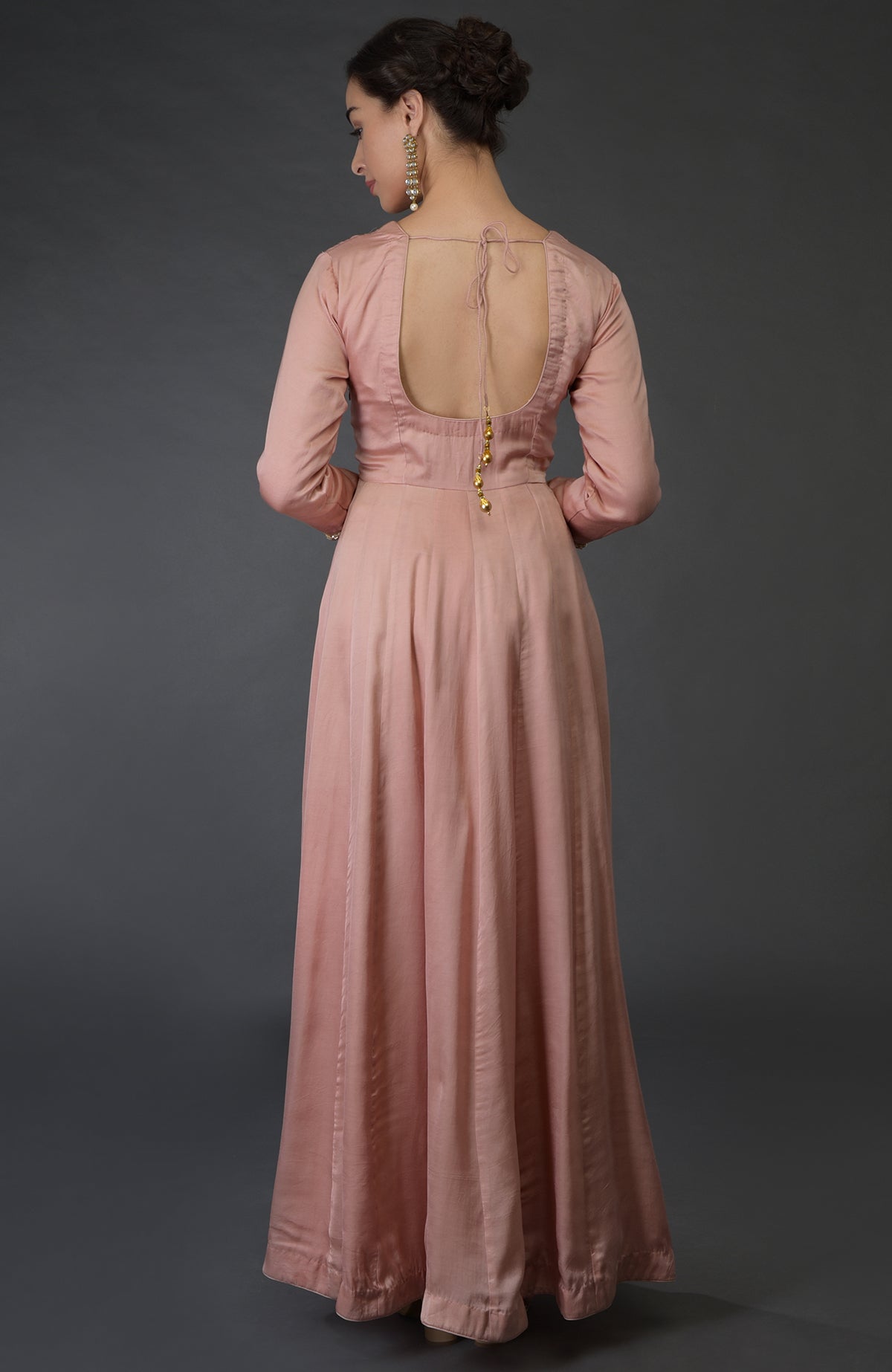 A woman in a pressed rose anarkali suit with a deep back and long earrings.