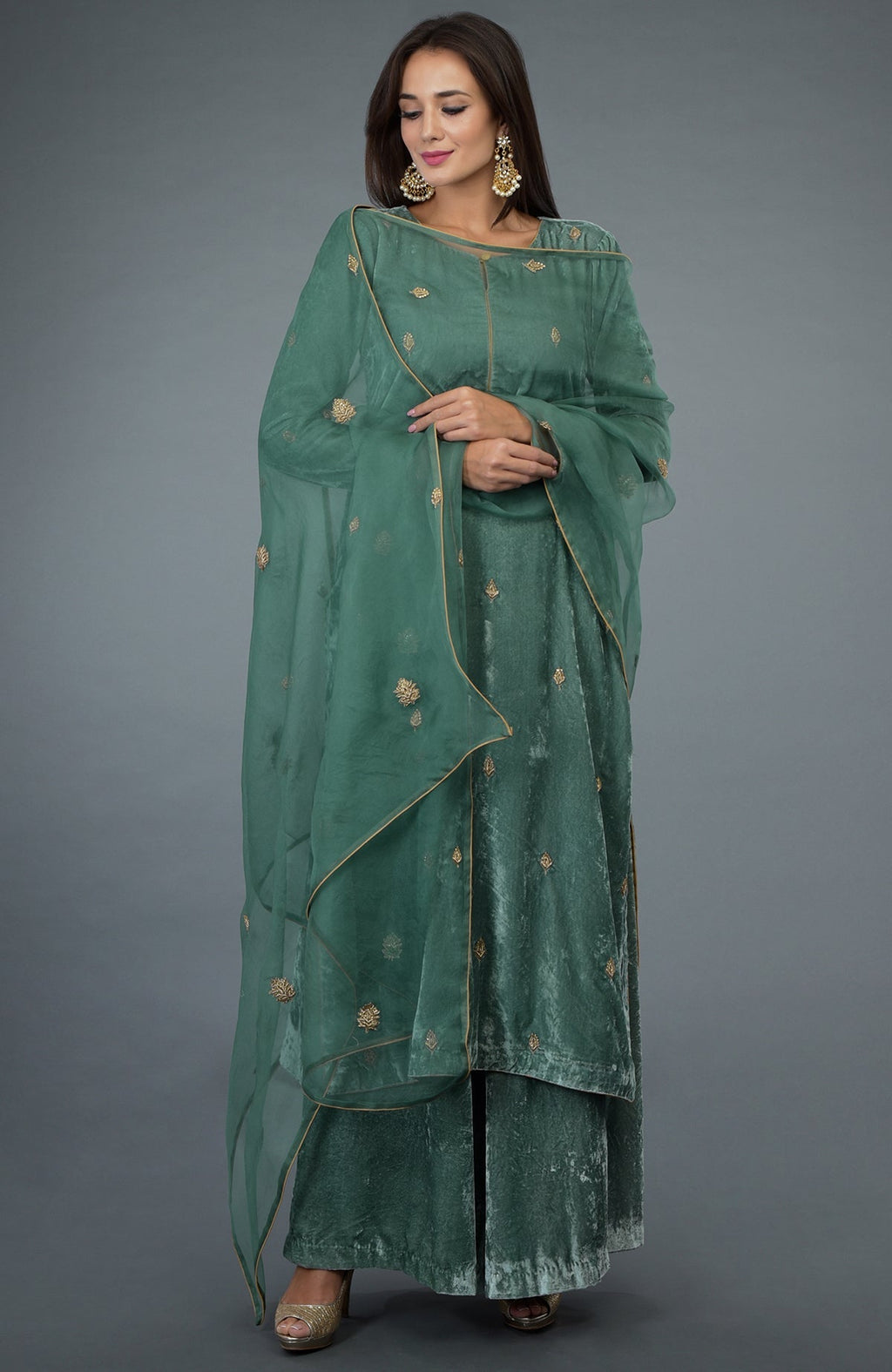 A woman models a jade green velvet suit with gold embroidery and an organza dupatta.