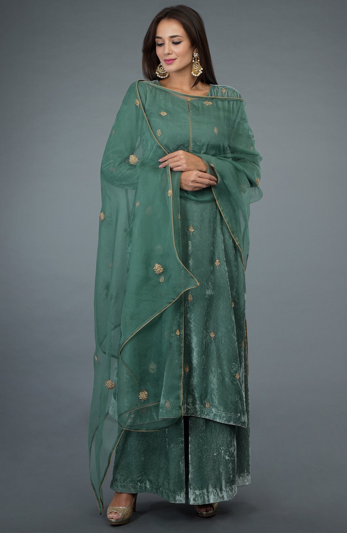 A woman models a jade green velvet suit with gold embroidery and an organza dupatta.