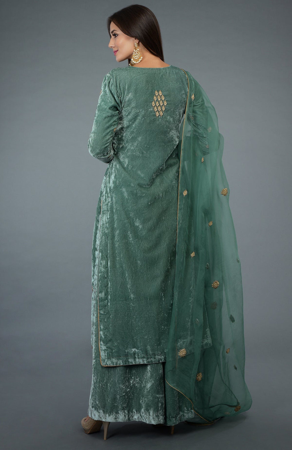 A woman models a jade green velvet suit with gold embroidery and a sheer dupatta.