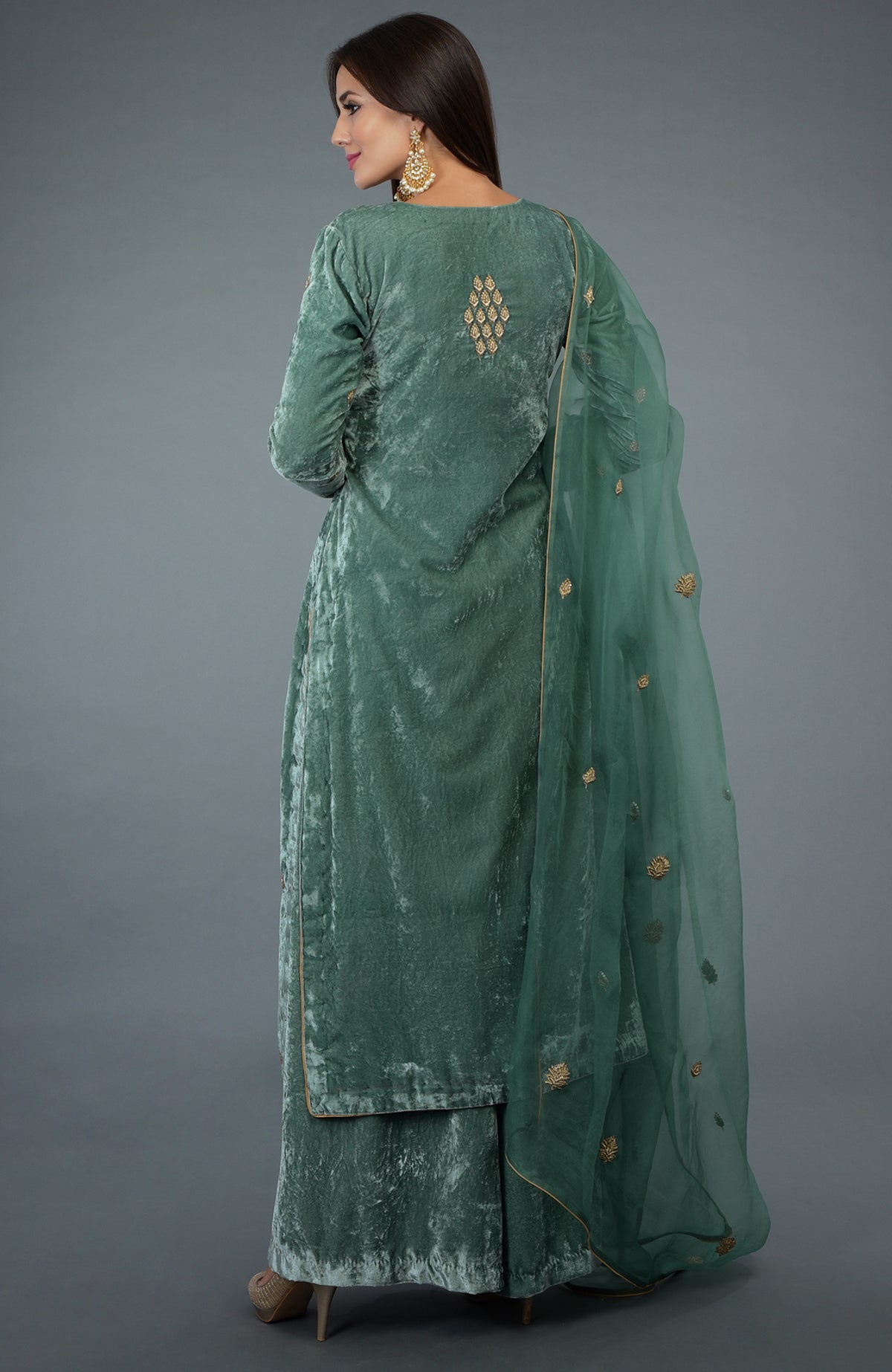 A woman models a jade green velvet suit with gold embroidery and a sheer dupatta.