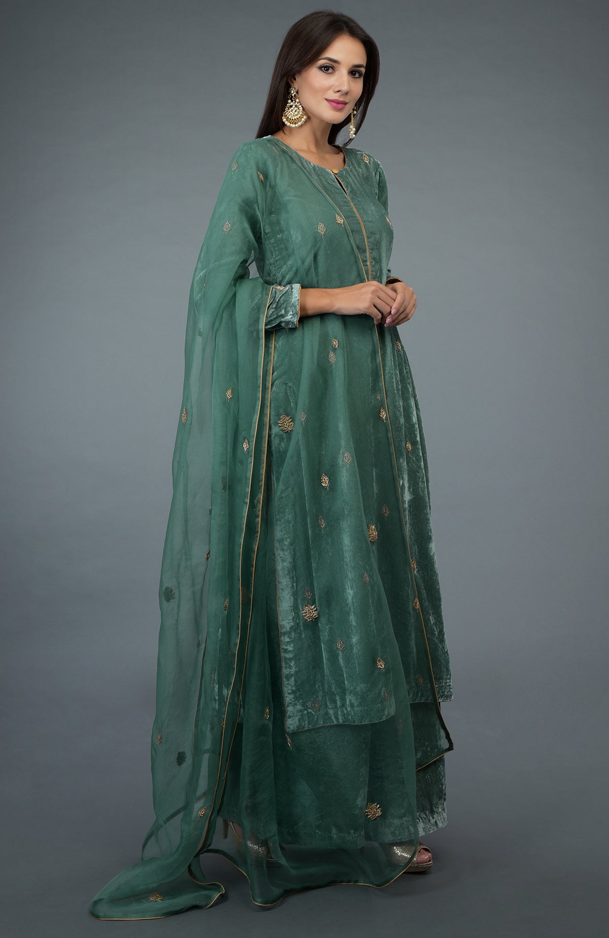 A woman models a jade green silk velvet suit with gold embroidery and an organza dupatta.