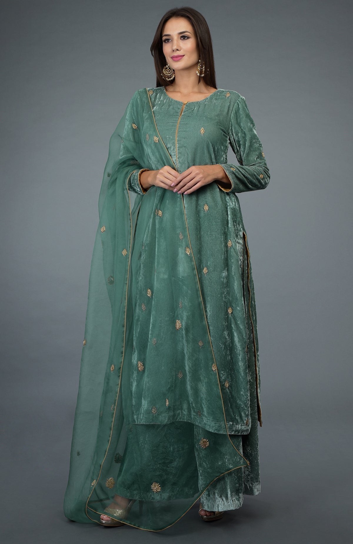 A woman models a jade green velvet suit with gold embroidery and a sheer dupatta.