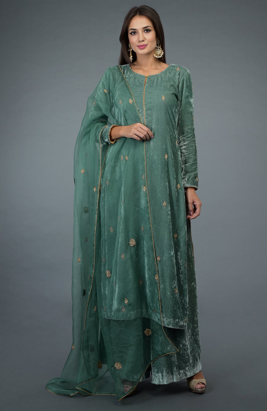 A woman models a jade green silk velvet suit with gold embroidery and a sheer dupatta.