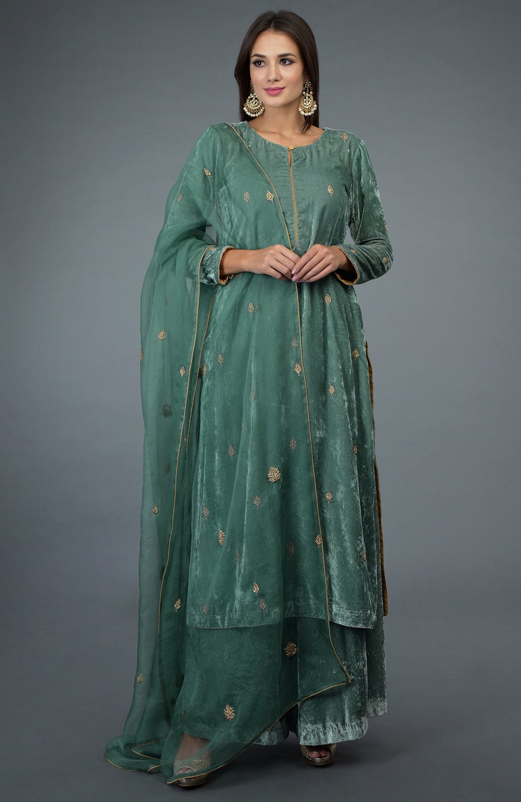 A woman models a jade green velvet suit with gold embroidery and a sheer dupatta.