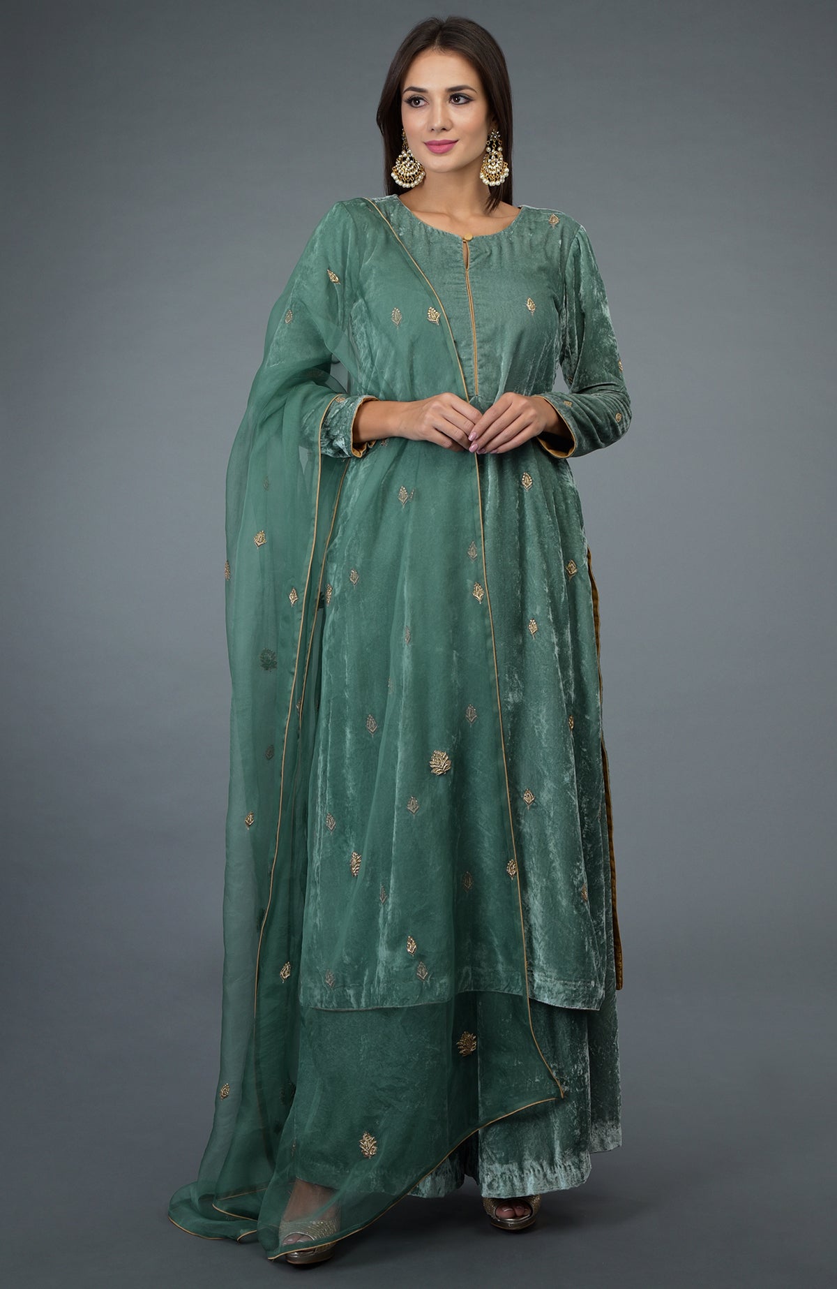 A woman models a jade green velvet suit with gold embroidery and a sheer dupatta.