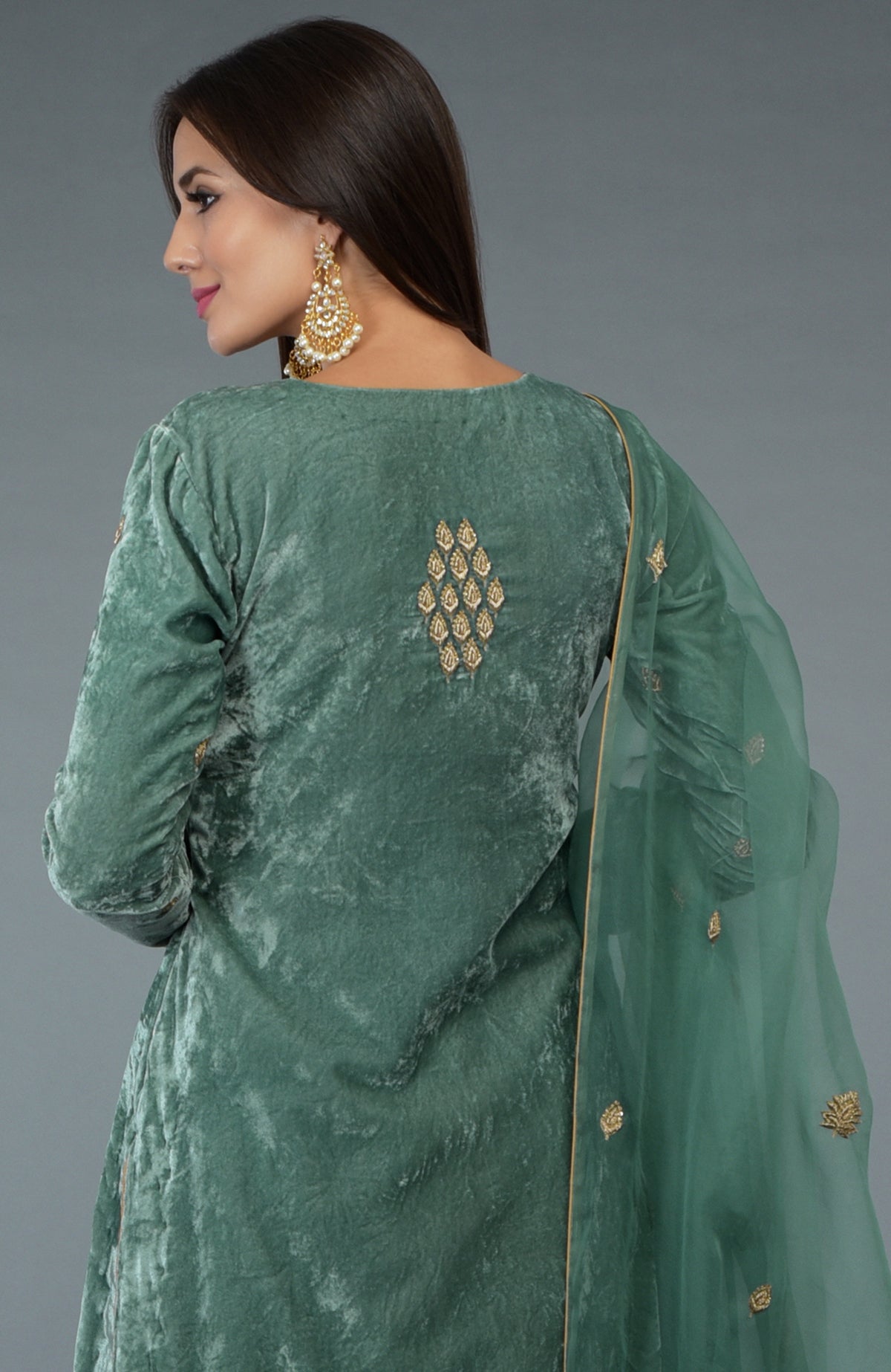 A woman models a jade green velvet suit with gold embroidery and a sheer dupatta.
