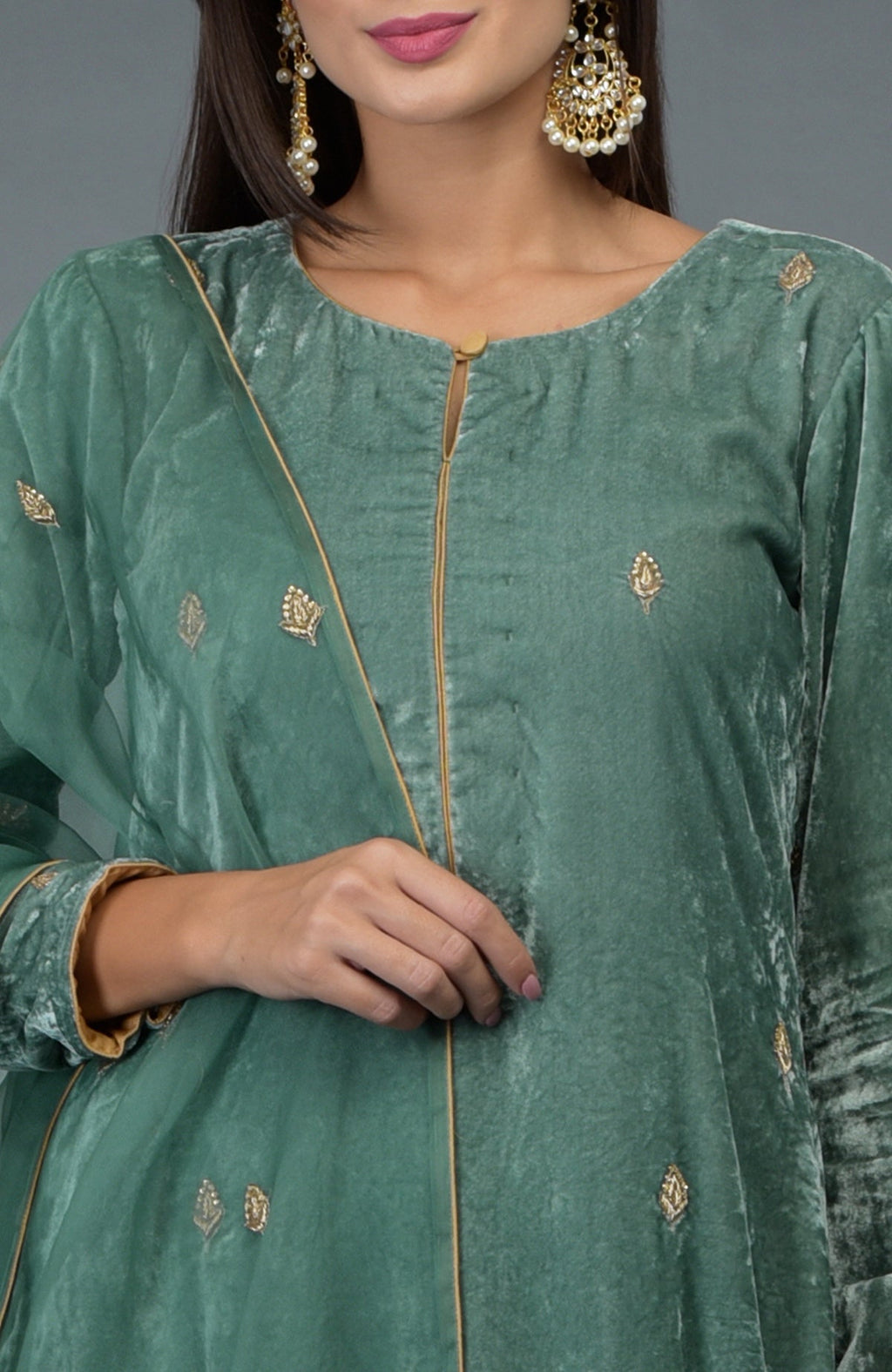 A woman models a jade green velvet suit with gold embroidery and pearl earrings.