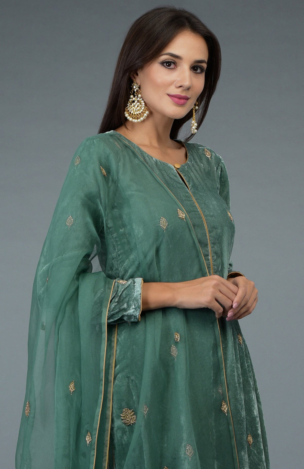 A woman models a jade green silk velvet suit with gold embroidery and pearl earrings.