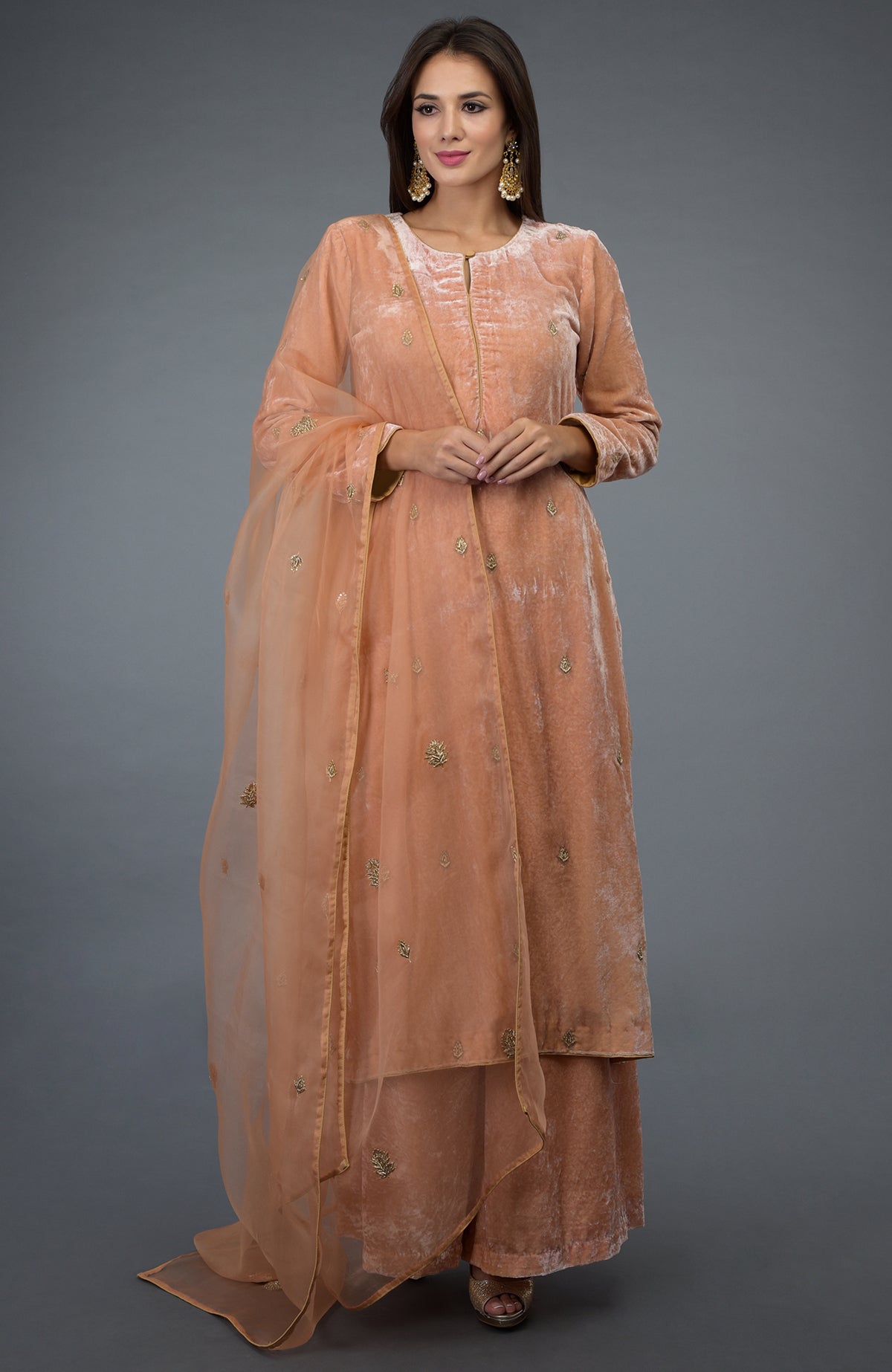 A woman models a peach rose zardozi hand-embroidered silk velvet suit.
