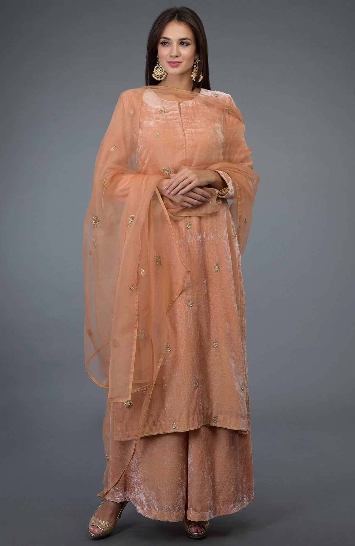 A woman models a peach rose zardozi hand-embroidered silk velvet suit.