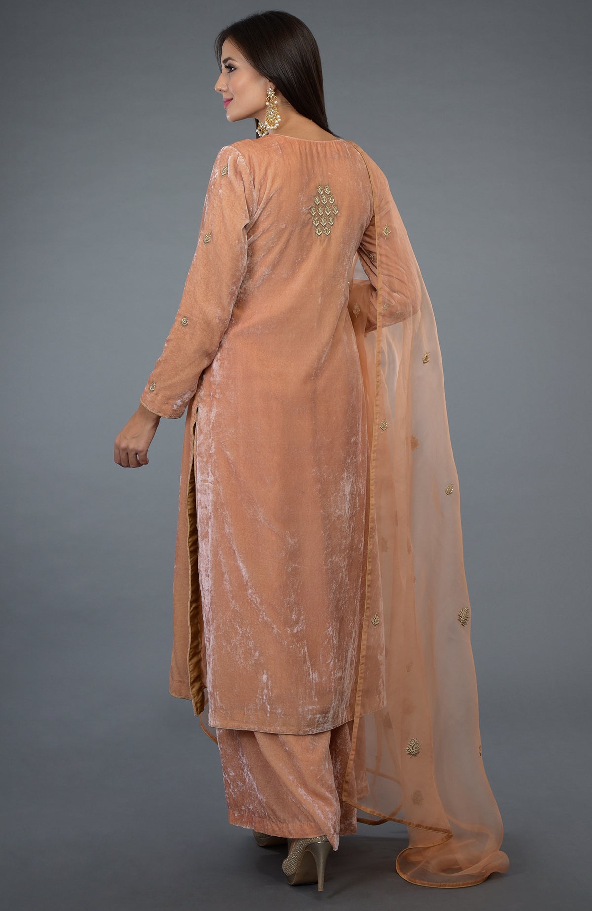 A woman models a peach rose silk velvet suit with zardozi embroidery and a sheer dupatta.