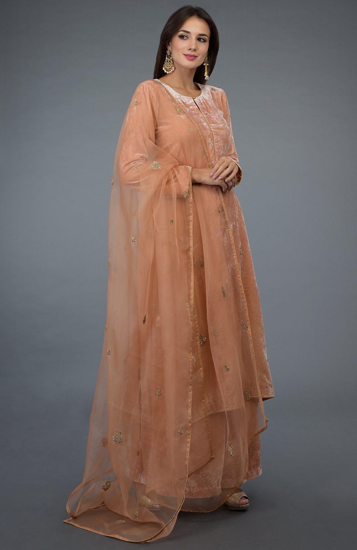 A woman models a peach rose zardozi hand-embroidered silk velvet suit with a sheer dupatta.