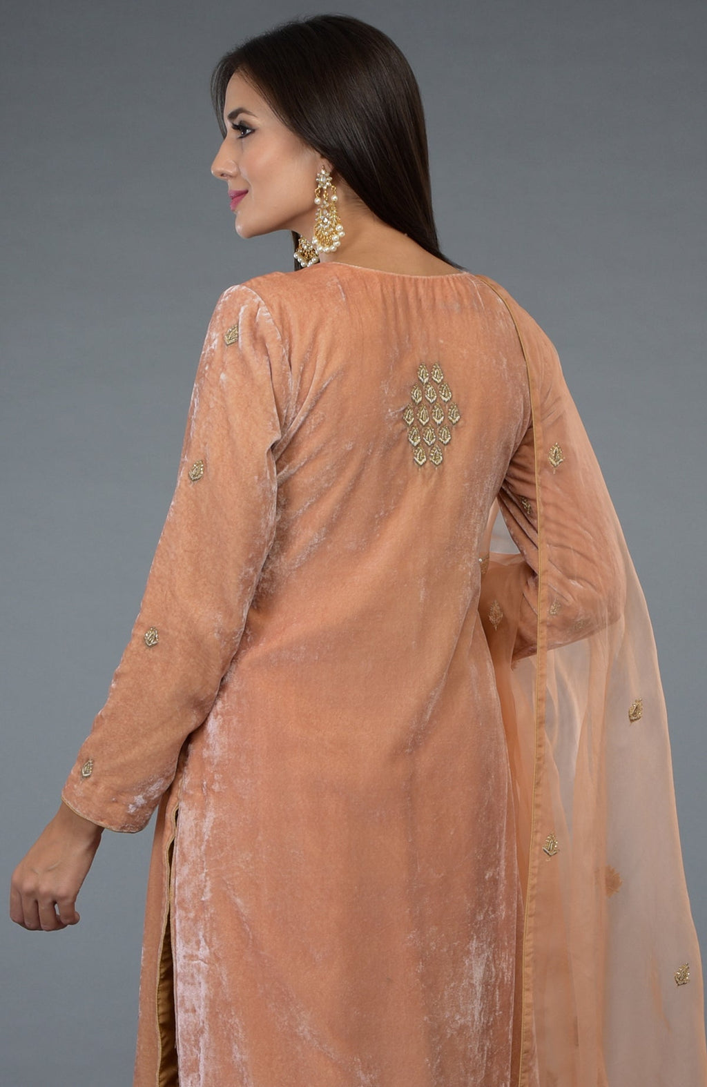A woman models a peach rose velvet suit with gold embroidery and a sheer dupatta.